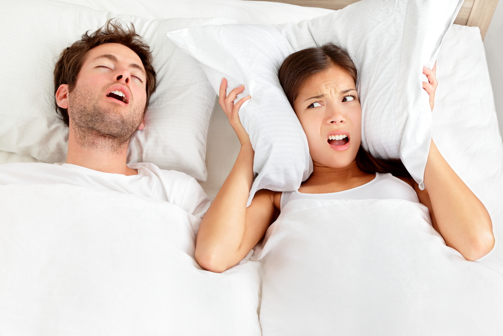 man snoring and woman covering her ears with a pillow